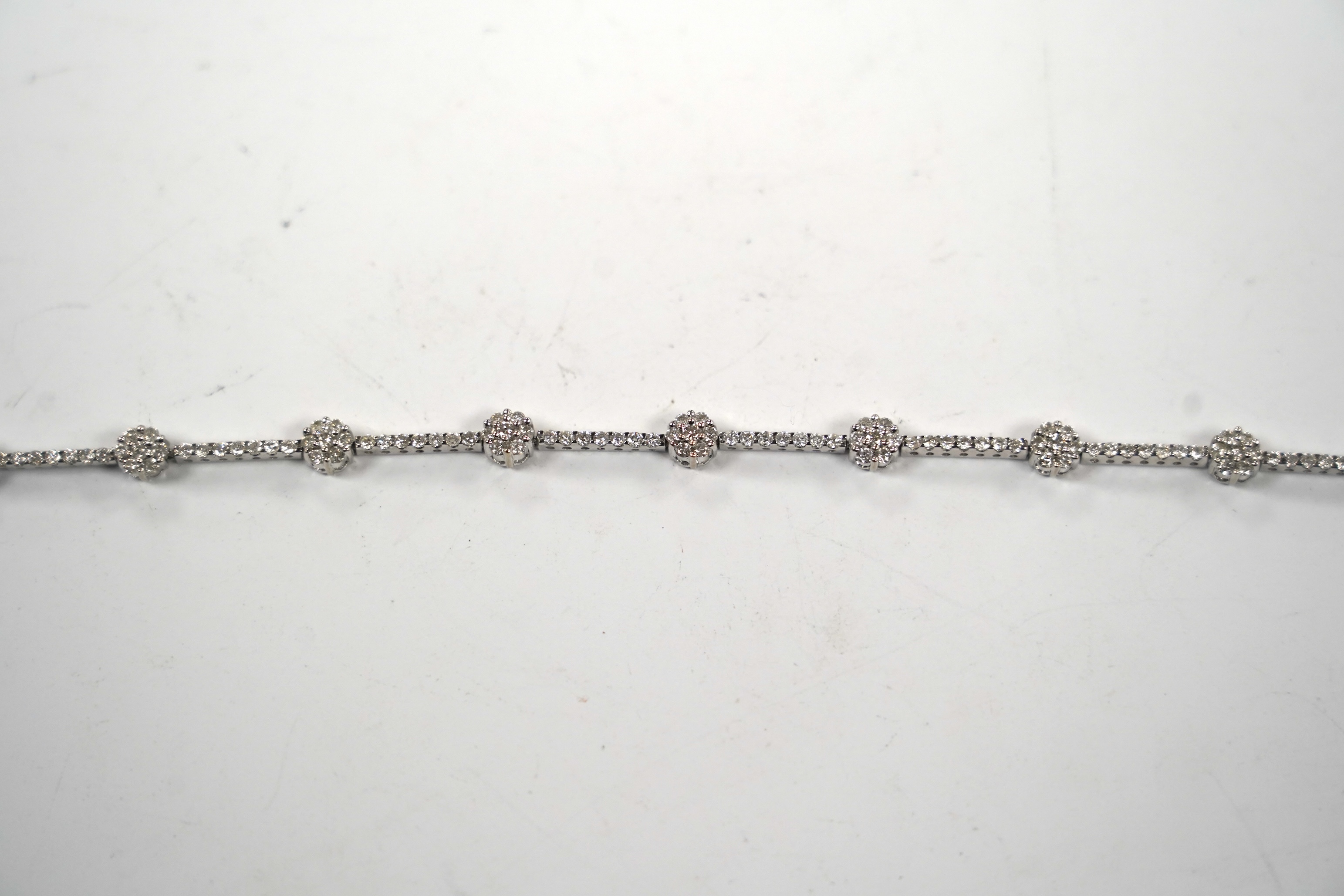 A modern 18k white metal and diamond cluster set line bracelet, 17.8cm, gross weight 8.8 grams.